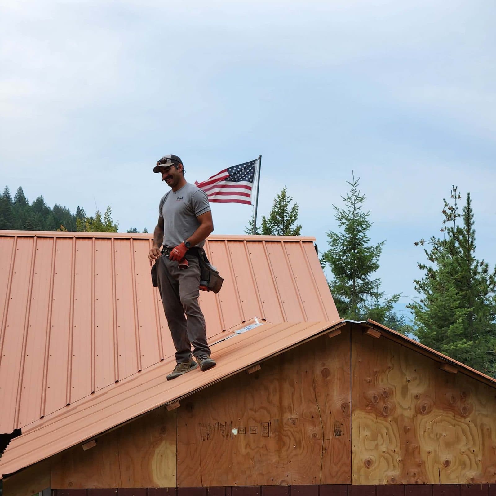 Brandon Ritchie, founder of Metal Roof Idaho, on a standing-seam metal roof in North Idaho under an American flag